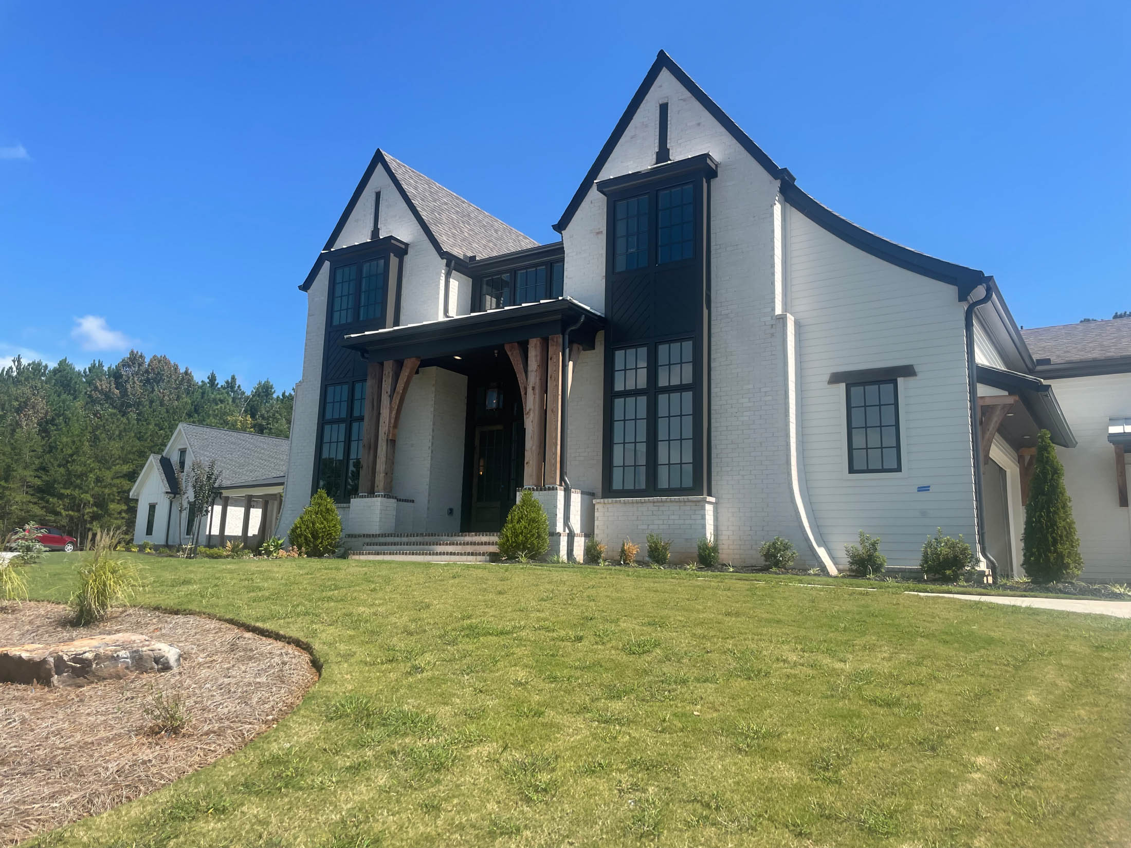 Two-story modern farmhouse with white brick exterior, dark trim, and wooden beams at the entrance, showcasing the quality craftsmanship you can expect when learning about Arreguin’s Paint Contractor.