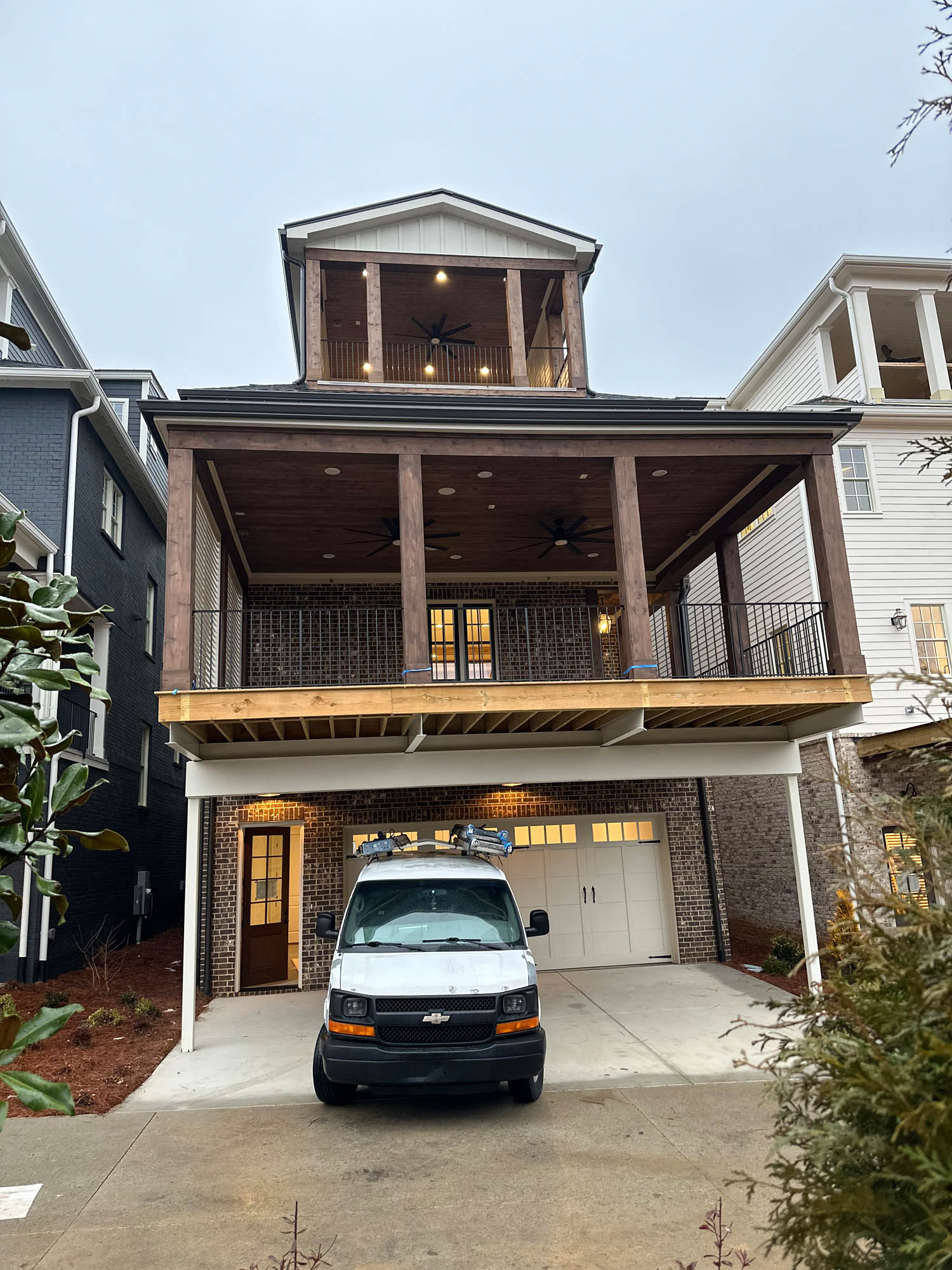A two-story brick house with a large covered balcony and a white garage door, with a white work van parked in the driveway.