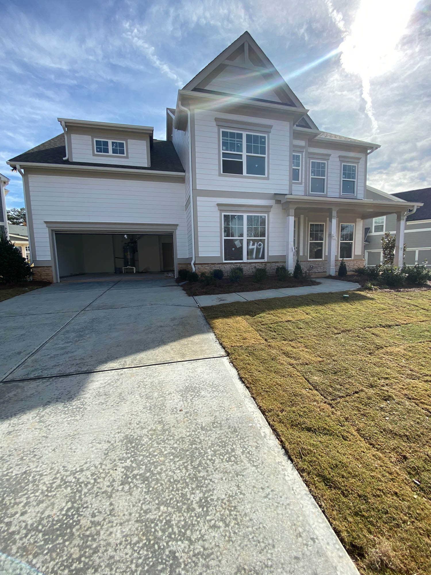 A two-story white house with a double garage, large front windows, and a concrete driveway, with a patch of new grass in the front yard.