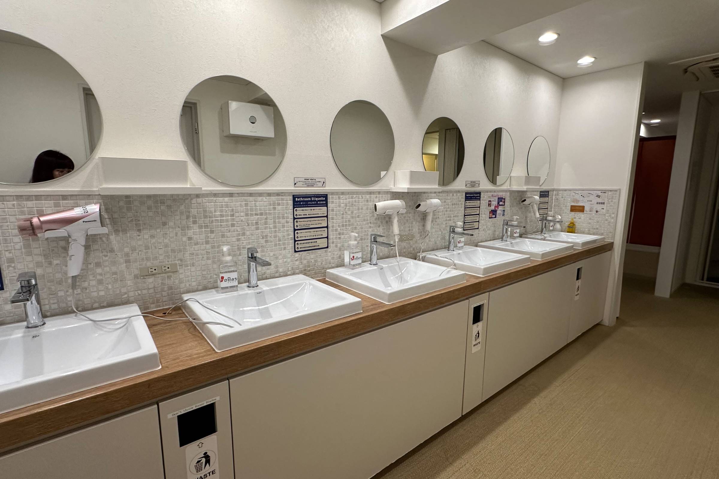 A row of five sinks with mirrors, hairdryers, and hand dryers in a clean, well-lit public restroom showcases quality new construction painting.