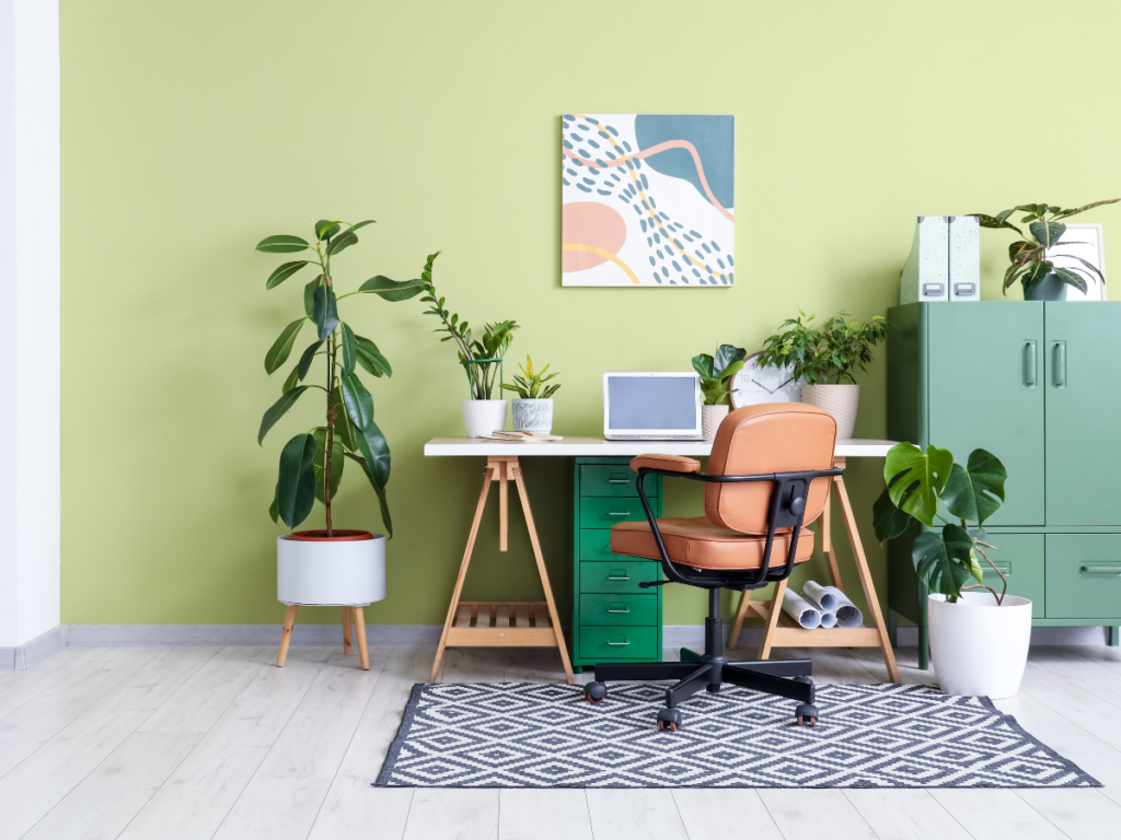 Modern home office with a wooden desk, potted plants, a computer, and abstract art—choose this soothing green paint color to bring fresh style and personality to your home workspace.